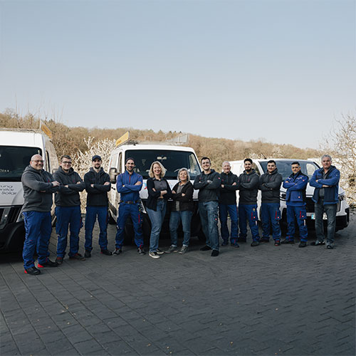Eine Gruppe von 11 Personen posiert lächelnd vor zwei weißen Lieferwagen im Freien.